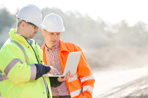 safety and site supervisors on a construction site looking at paperwork on a screen