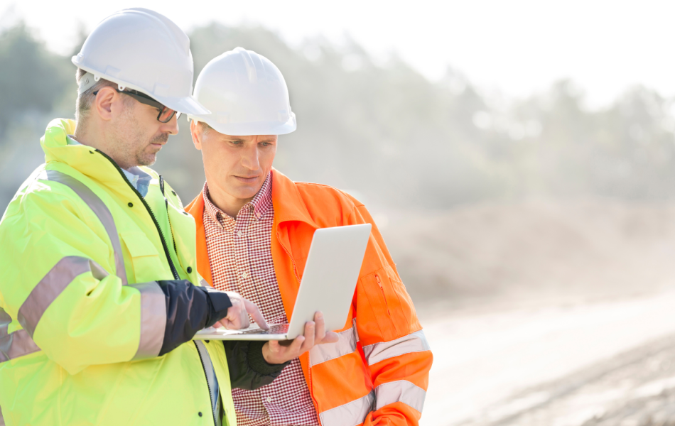 safety and site supervisors on a construction site looking at paperwork on a screen